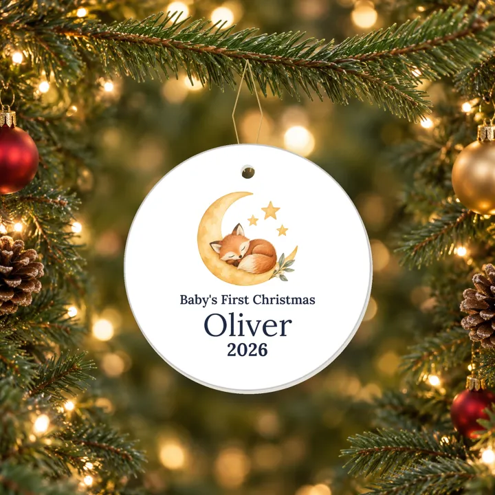 Ceramic Baby's First Christmas 2026 ornament with a moon and fox and a sample name, hanging on a tree